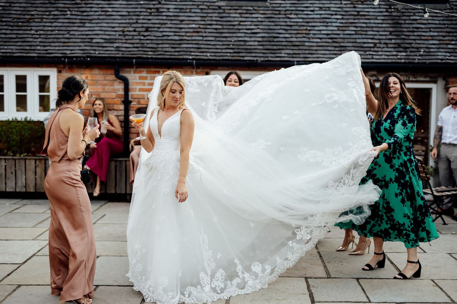 A flowing white wedding dress billows in the wind as guests gather outside.