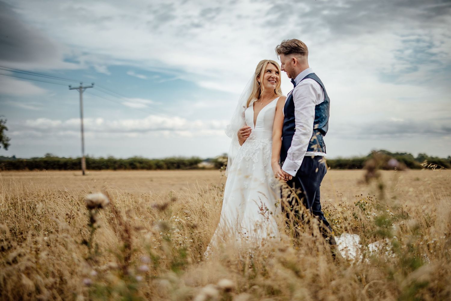 Wedding couple embraces in a golden wheat field during sunset.
