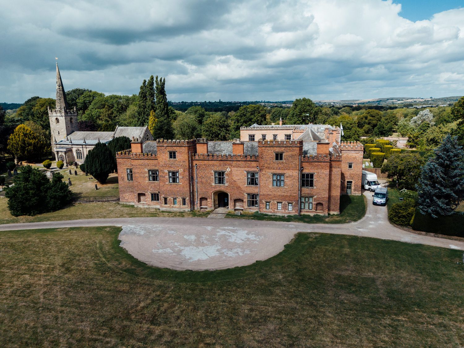 Aerial panoramic view of a historic red brick estate venue surrounded by manicured grounds.