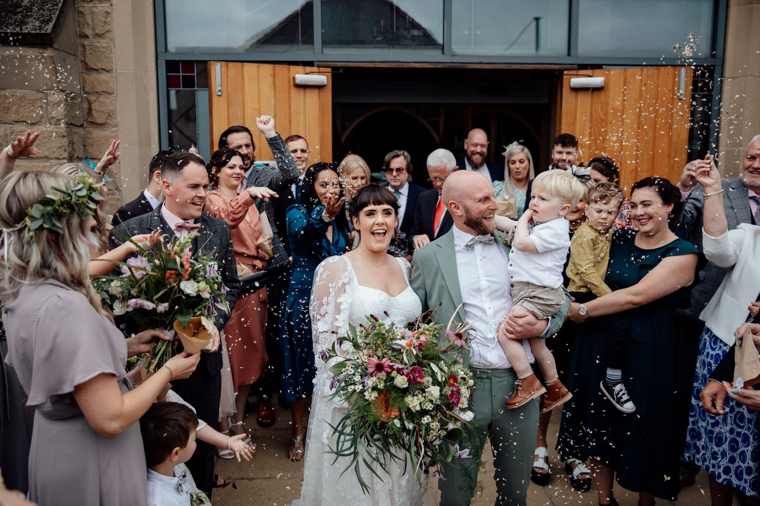 Wedding celebration outside a rustic stone and wooden barn with floral decorations.