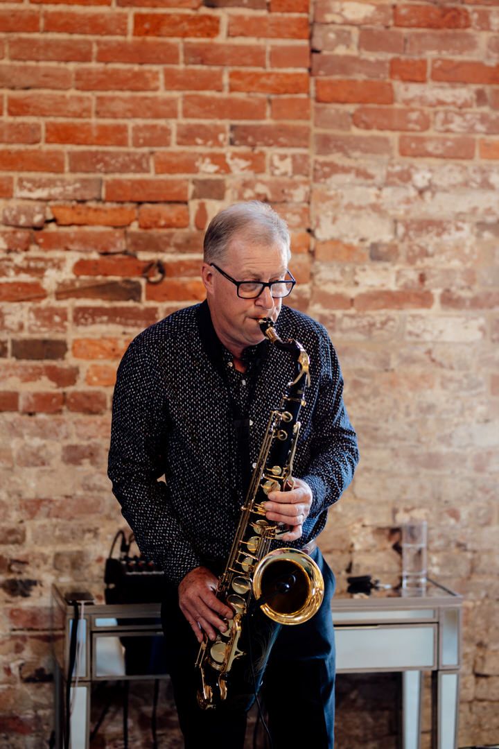 Saxophonist performing at a wedding reception against exposed brick wall backdrop.