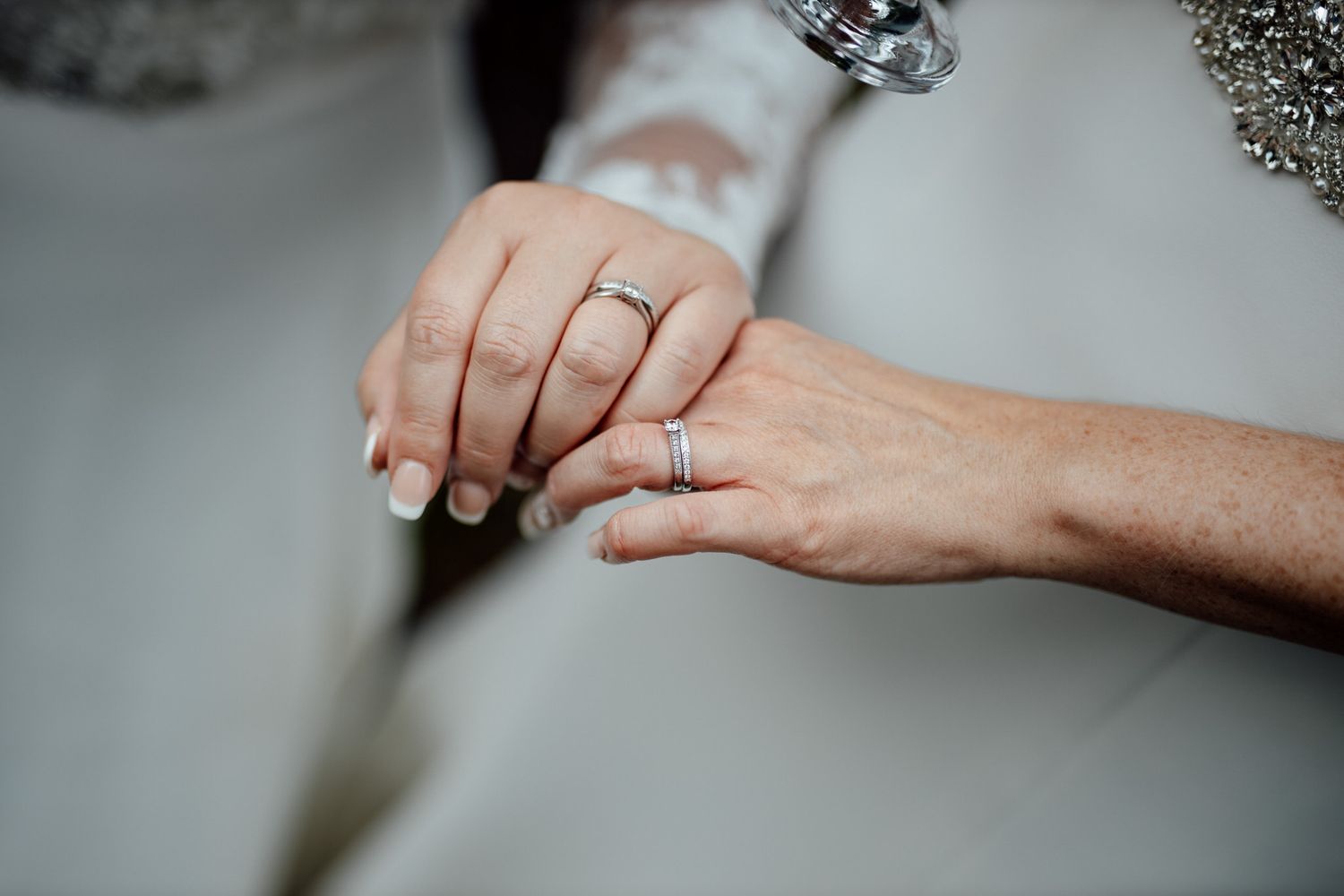 Close-up of elegant wedding rings and jewelry details on a light gray surface.