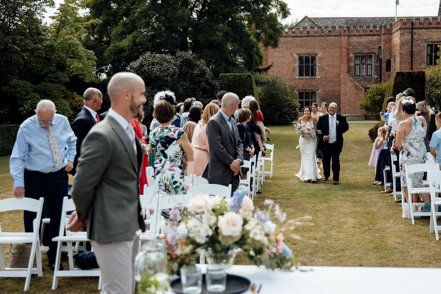 Outdoor wedding ceremony setup with white chairs and floral arrangements near historic building.