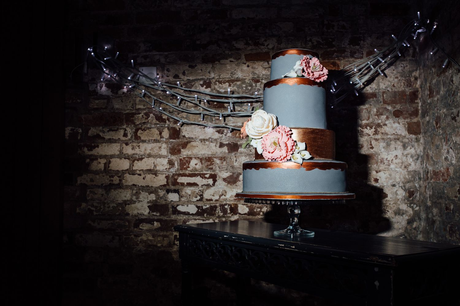 An elegant blue and pink wedding cake sits against a dramatic brick wall backdrop.