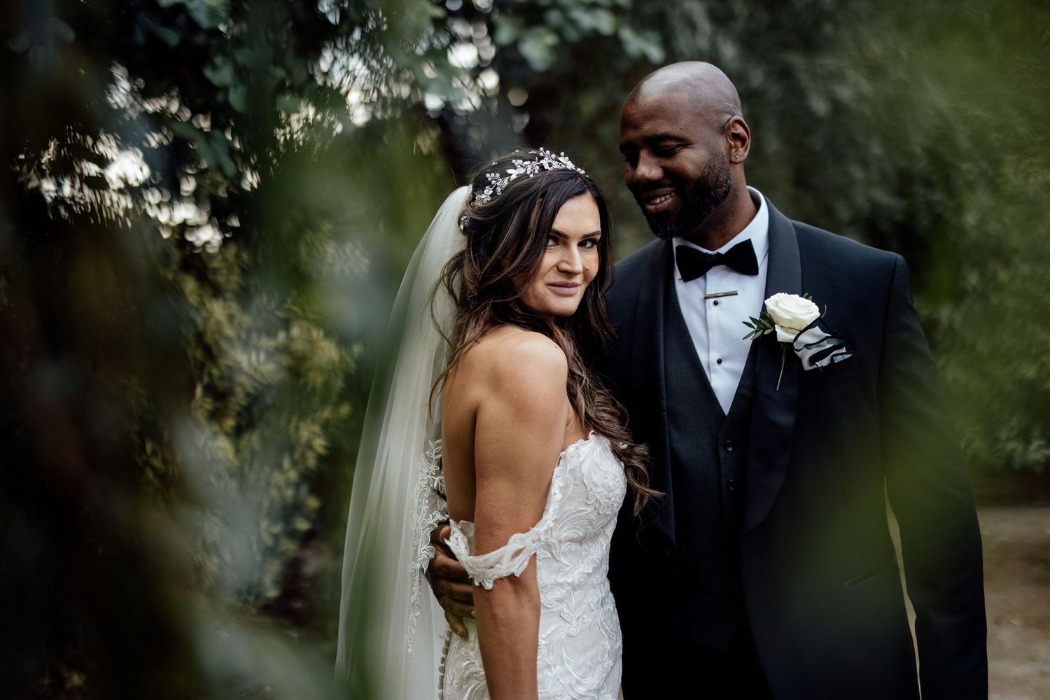 Romantic wedding portraits captured through natural foliage in garden setting.
