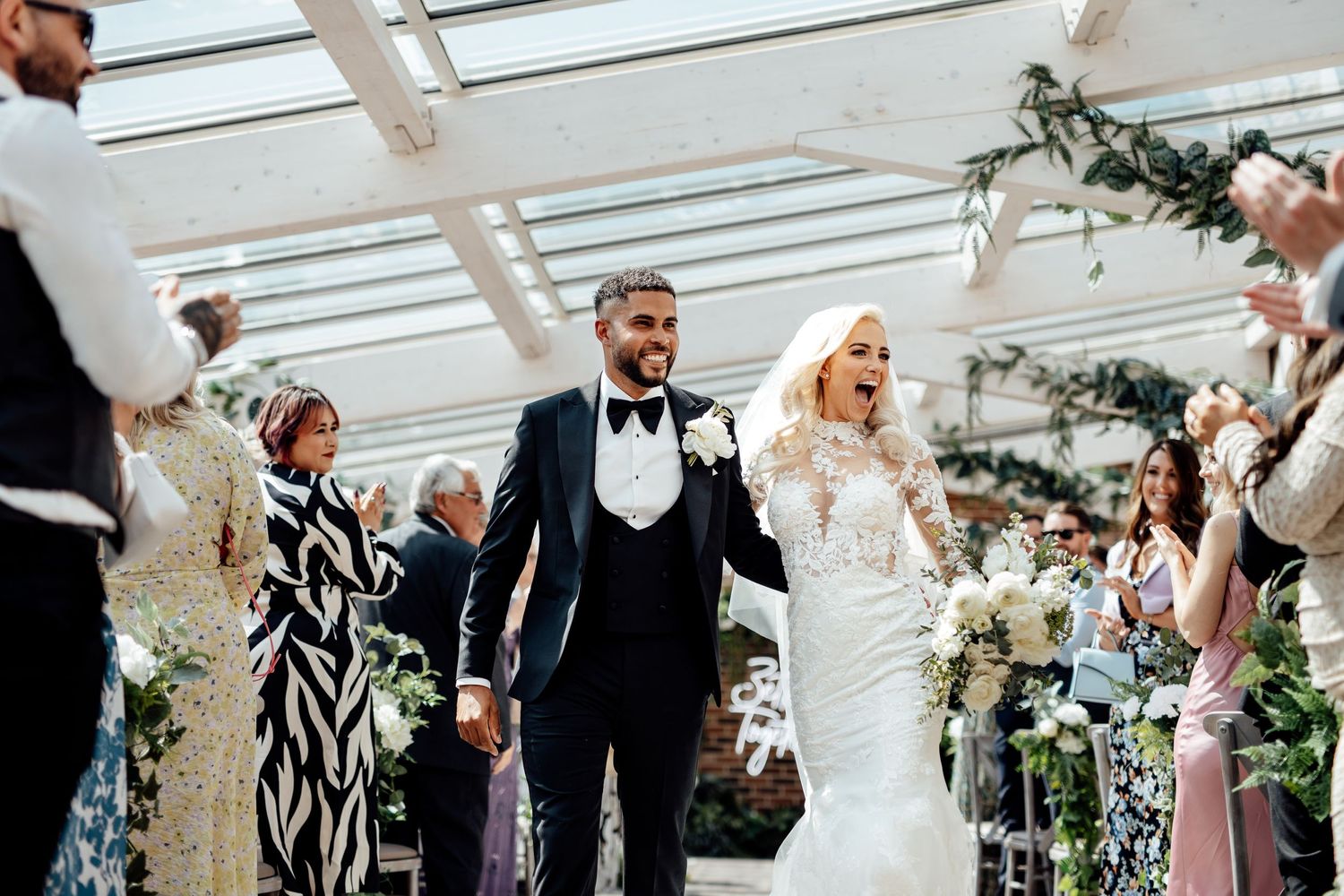 Wedding guests celebrate during an indoor reception with string lights and greenery decorations.
