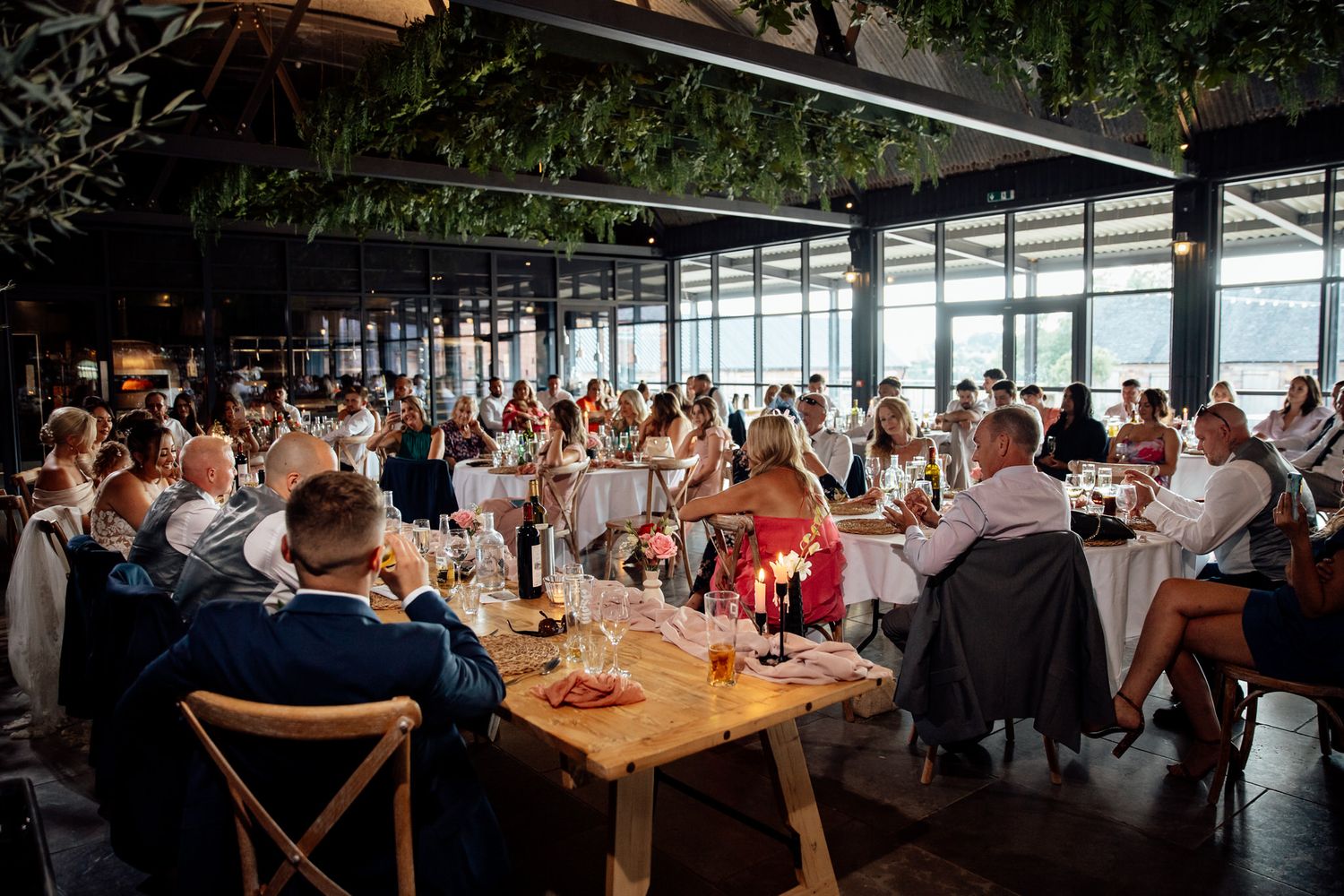 Large wedding reception dinner in modern venue with floor-to-ceiling windows overlooking city views.