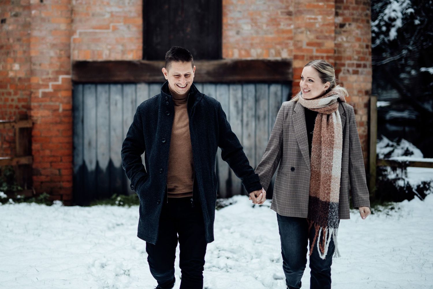 Winter engagement photos captured against rustic brick architecture in the snow.