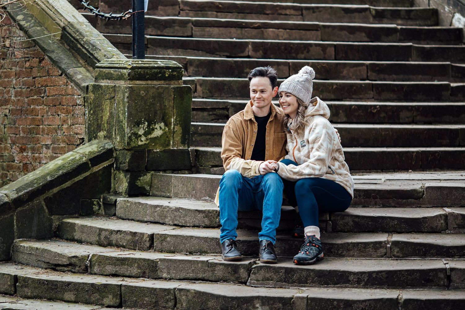 Couple sitting together on rustic stone steps in a park setting.