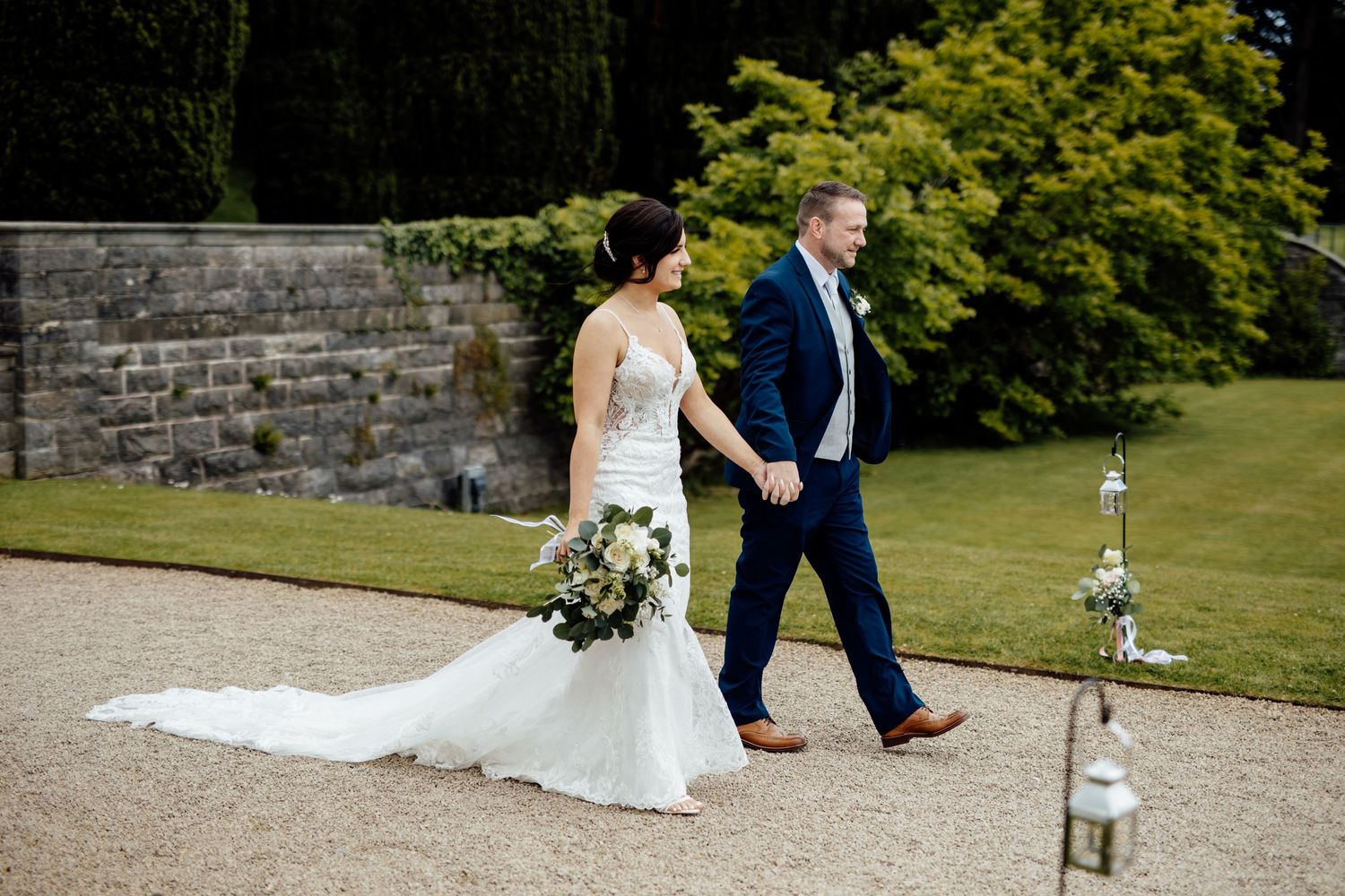 Wedding couple walking through garden grounds with decorative lanterns and stone paths.