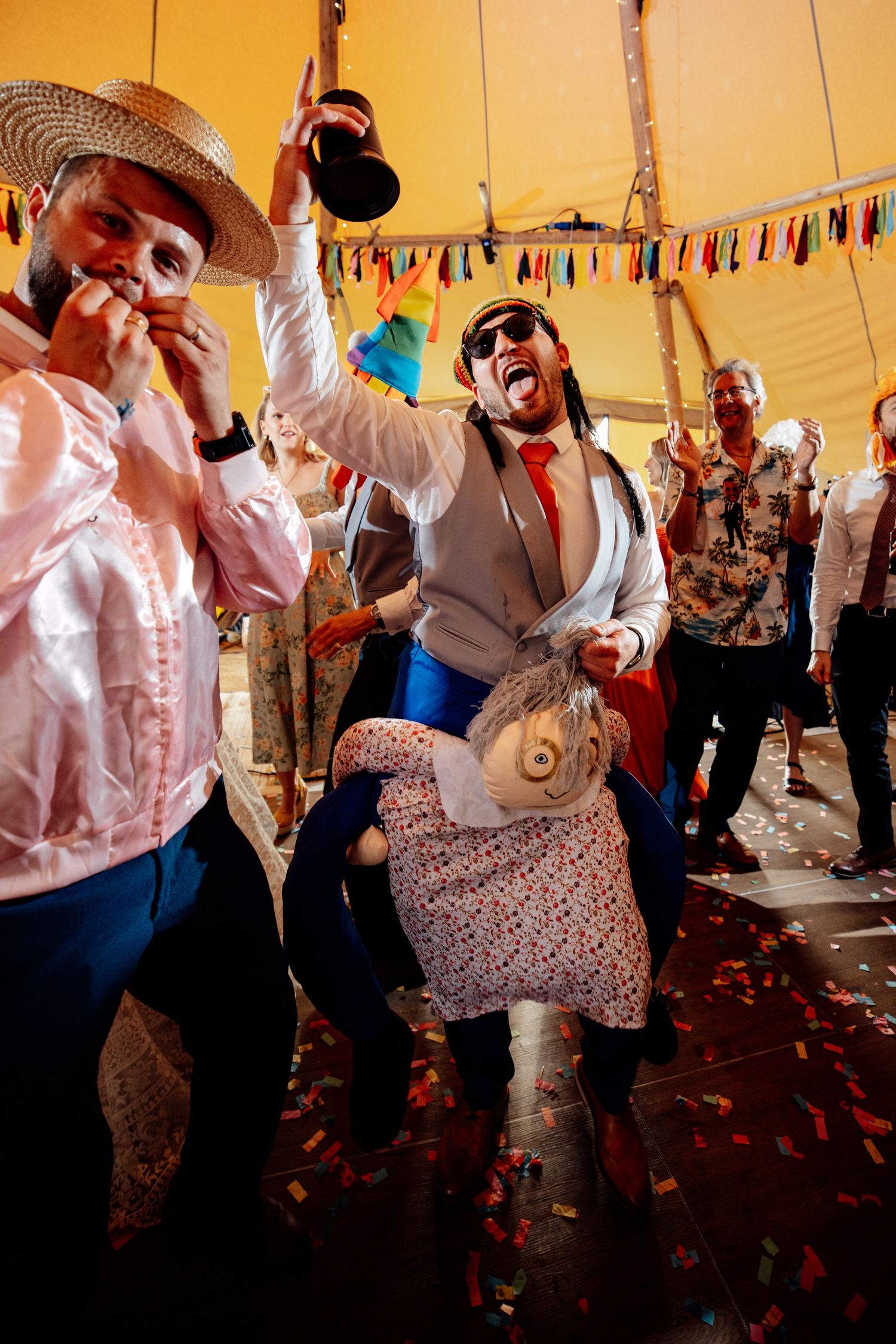 Wedding guests dance energetically under festive tent with colorful decorations.