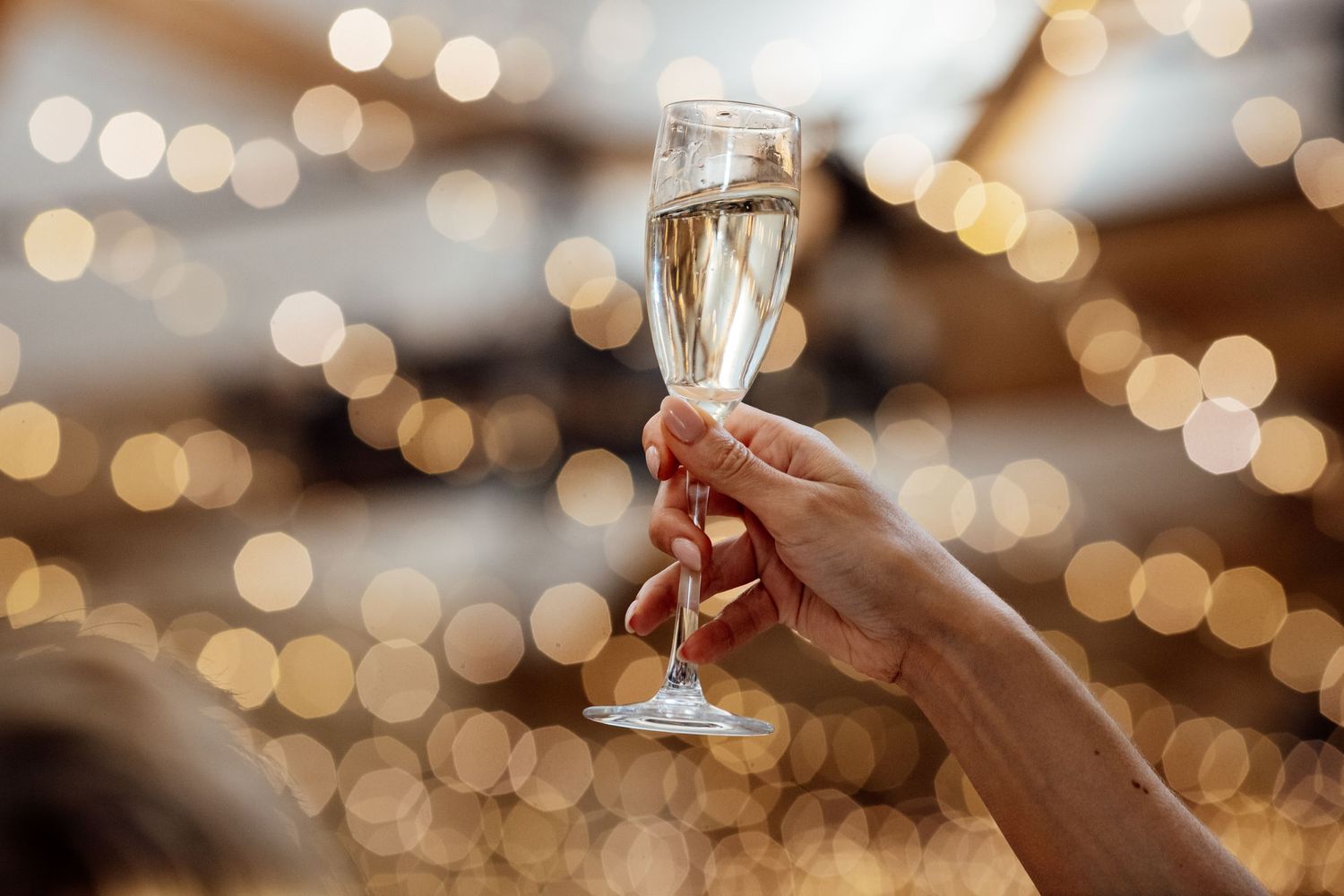 Hand holding up a champagne flute with sparkling bokeh lights in the background.