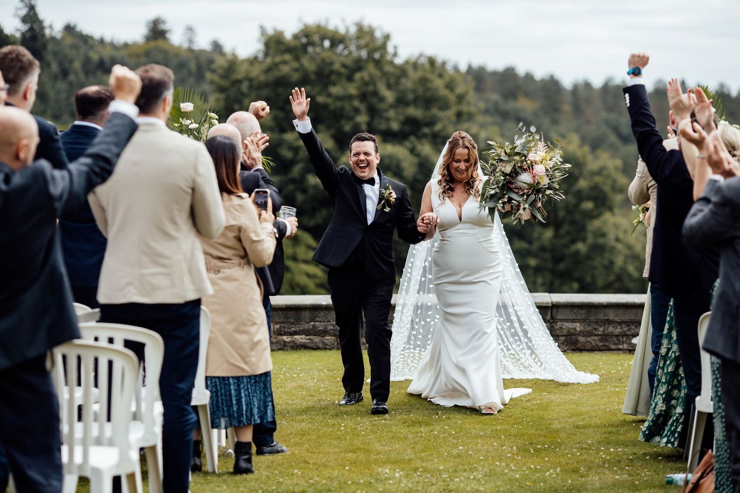 Outdoor wedding ceremony with guests seated on white chairs overlooking scenic landscape.
