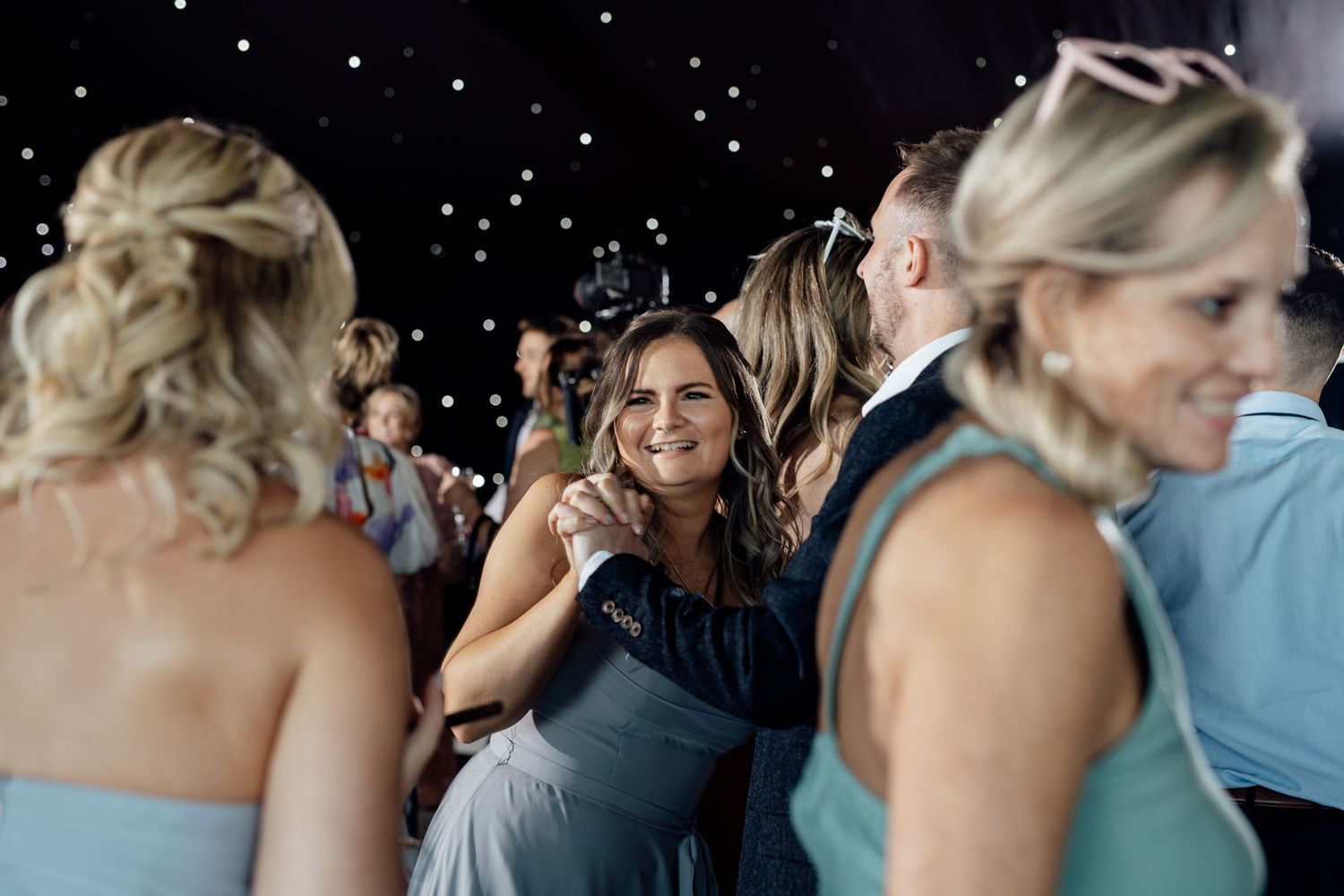 Wedding guests enjoying a celebration with twinkling lights in the background.
