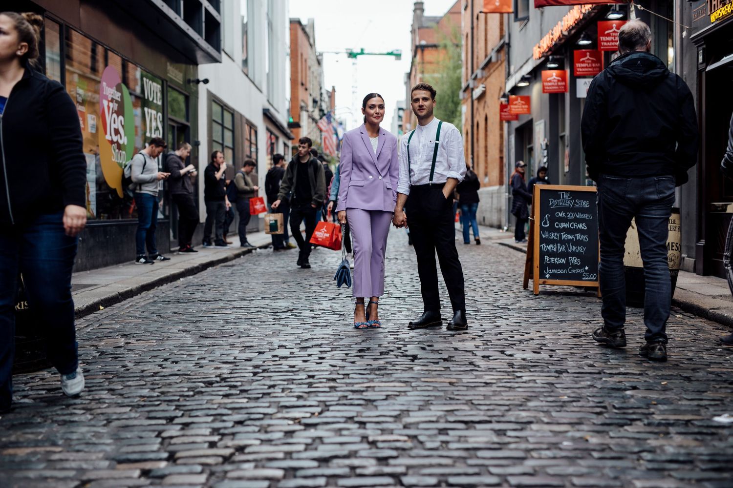 Couple walking together on a cobblestone street in stylish formal wear.