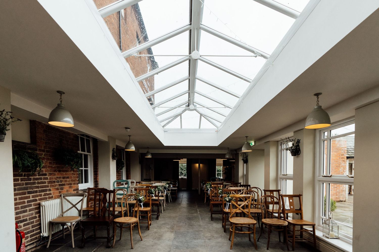 Modern restaurant interior with skylight ceiling, exposed brick walls and wooden furniture.