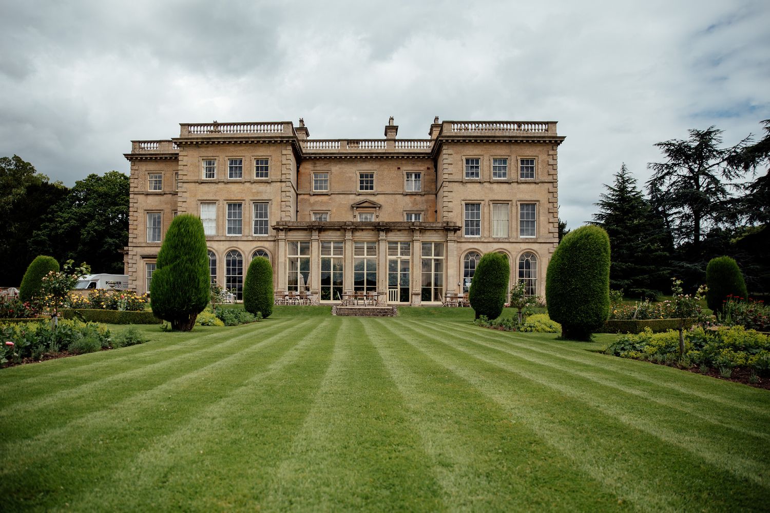 Panoramic view of a stately stone manor house with manicured green lawns.