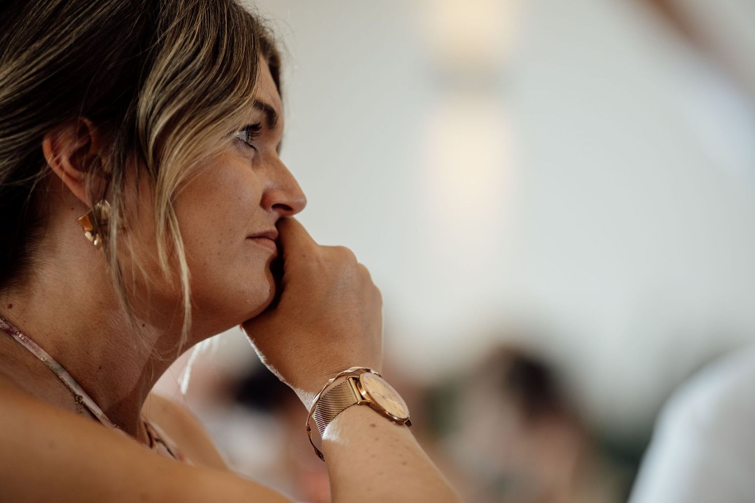 Woman in profile view wearing gold watch and earrings at a wedding reception.