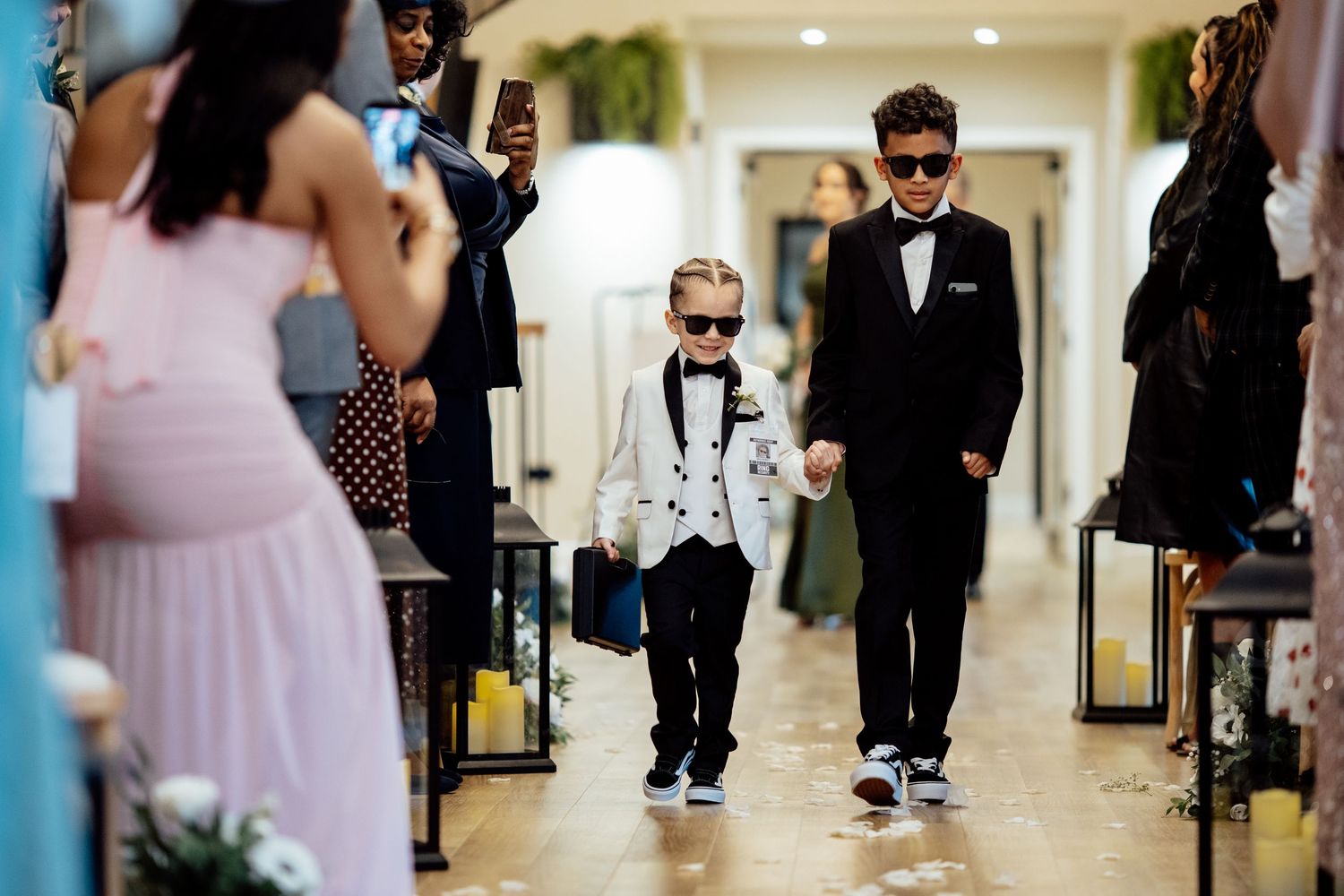 Two young boys in suits and sunglasses walking down wedding ceremony aisle.