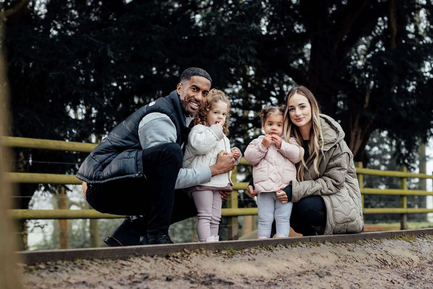 A family sits together on a grassy hill during an outdoor photo session at sunset.