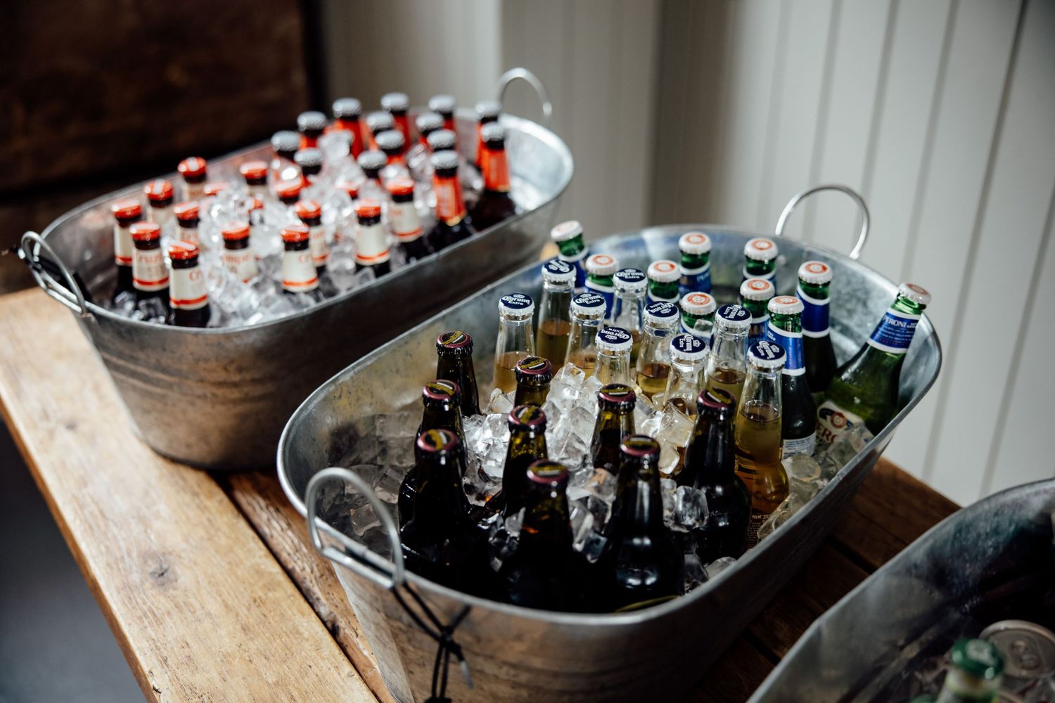 Bottles of beverages chilling in metal ice buckets at an event.