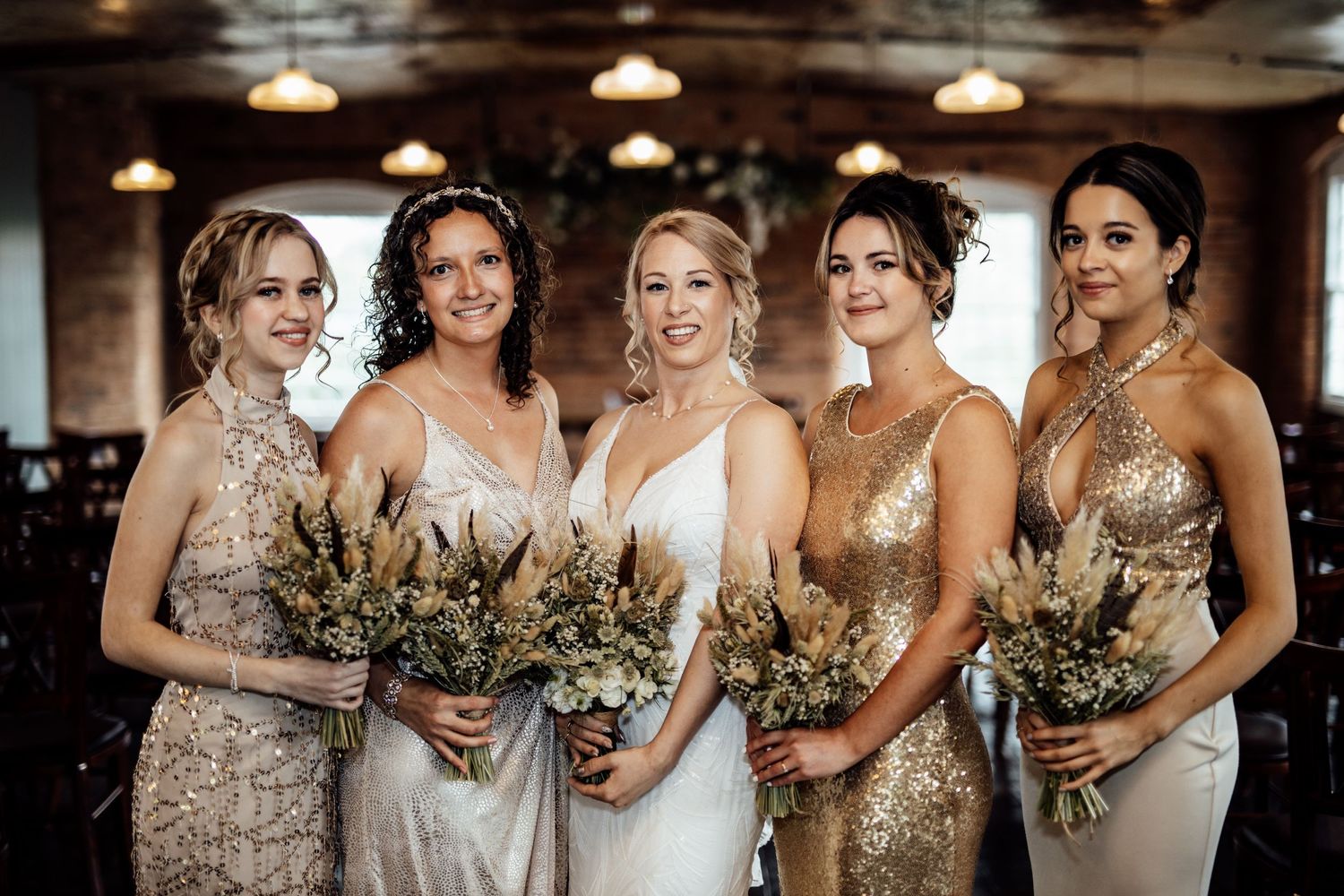Bridesmaids in sequined dresses gather for group photo in industrial-style venue.
