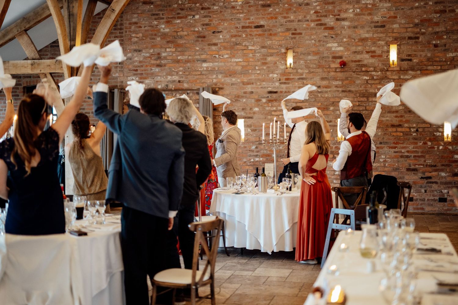 Elegant wedding reception venue with exposed brick walls, white tablecloths, and hanging pendant lights creating a rustic ambiance.