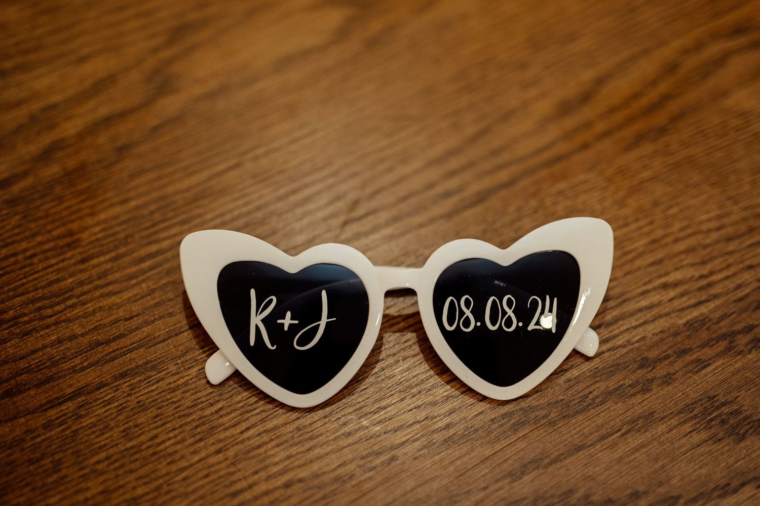 Decorative sunglasses with heart shapes and wedding details displayed on wooden surface.