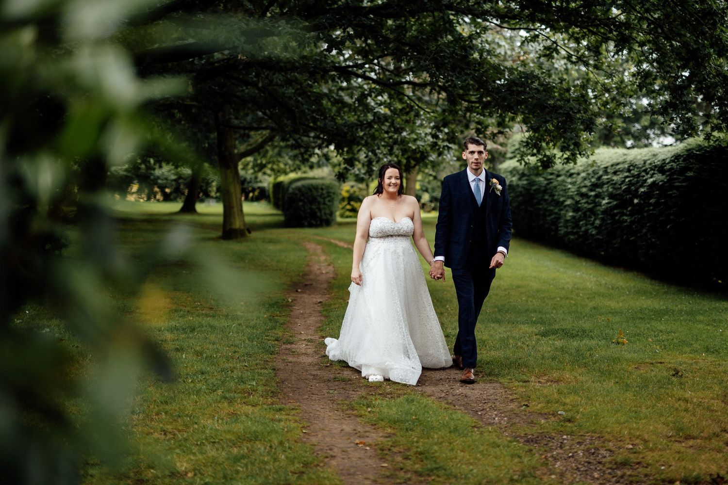 Wedding party walking through lush garden path during outdoor photo session.