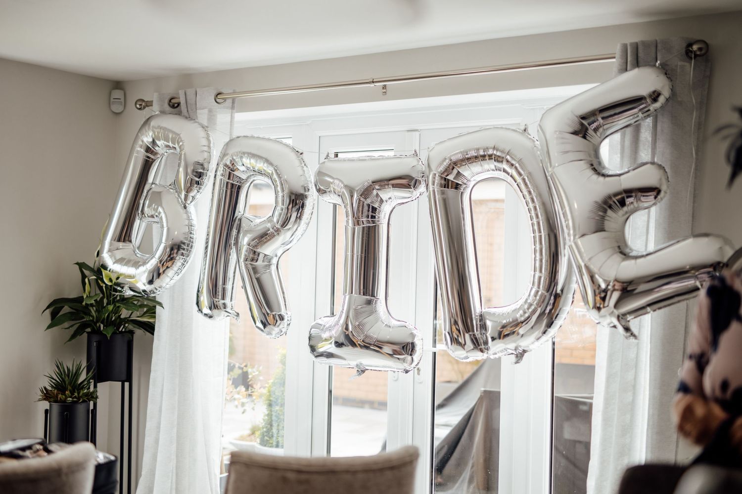 Silver letter balloons spelling 'BRIDE' decorate a bright white room with elegant lighting.
