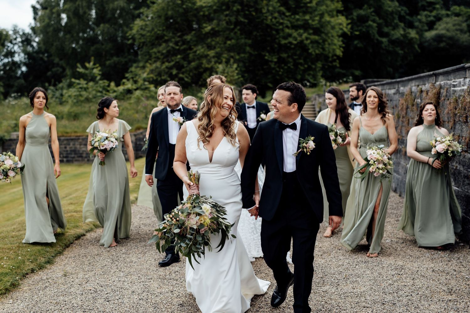 Wedding party walking and laughing together on a gravel path.