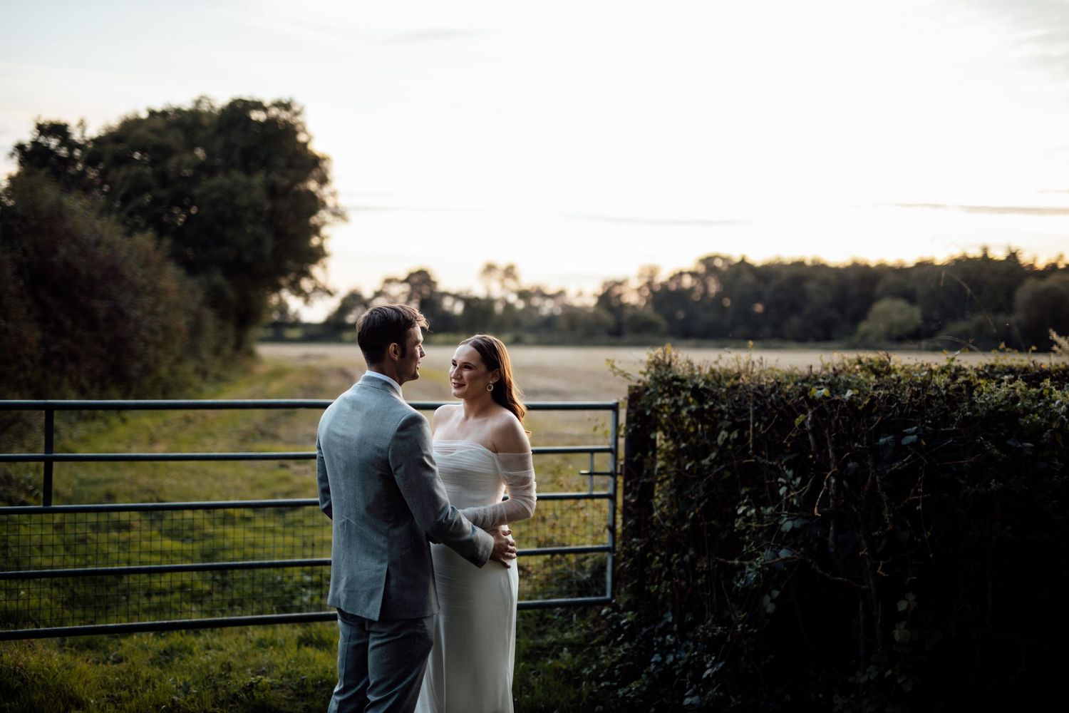 Newlyweds share an intimate moment at sunset against a countryside backdrop.