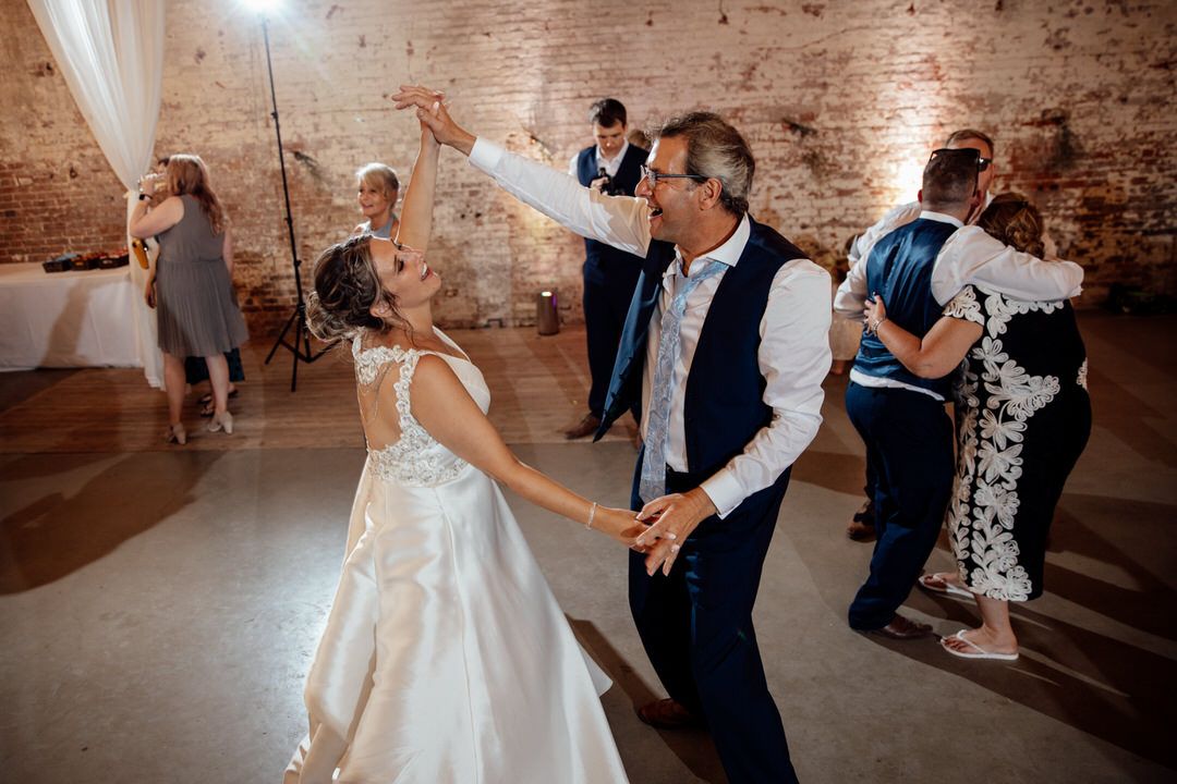 Couples dance together at wedding reception in rustic brick venue with elegant draping.
