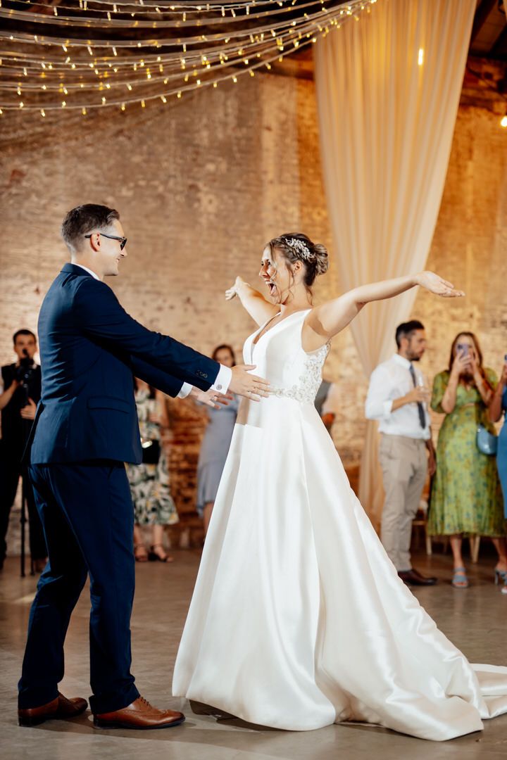 Couple dances under string lights in rustic brick venue.