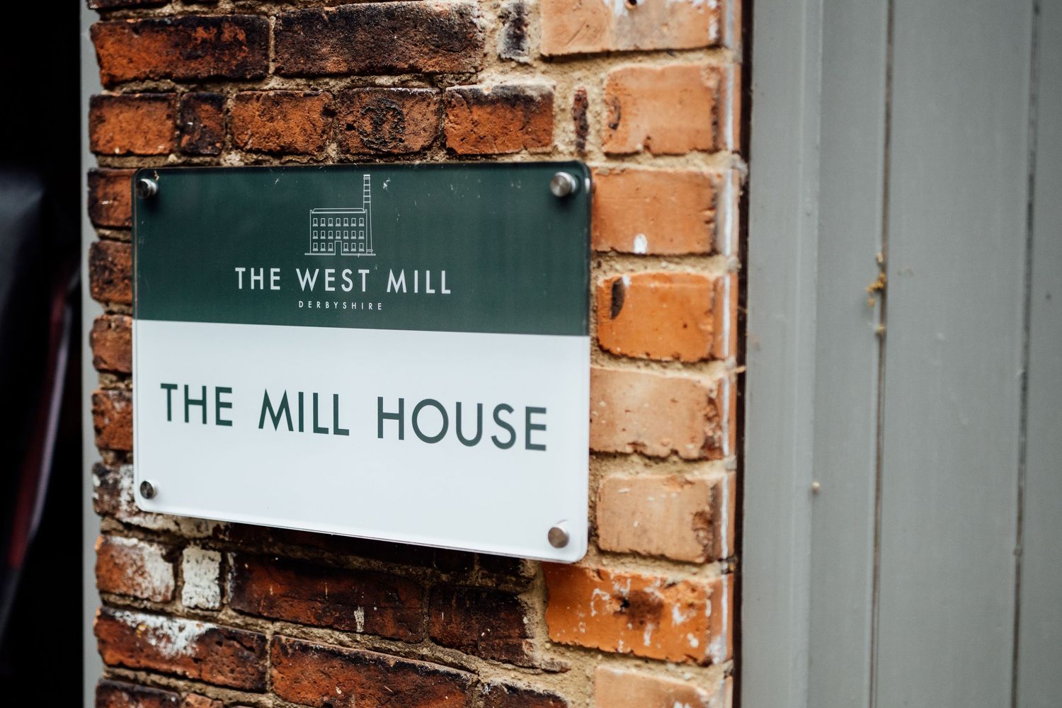 Rustic brick wall with mounted signage for 'The West Mill' and 'The Mill House' establishments.