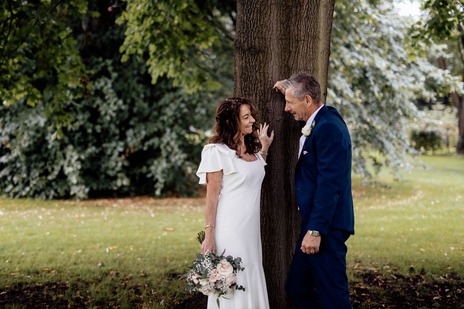 Couple walking together through lush green park setting.