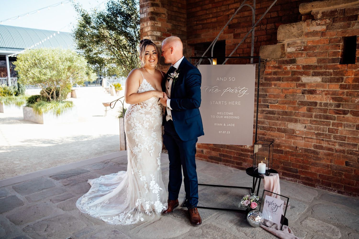 Couple poses against rustic brick wall backdrop during outdoor wedding photoshoot.