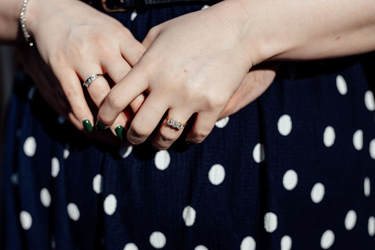 Close-up of hands with wedding rings against a navy and white polka dot fabric background.