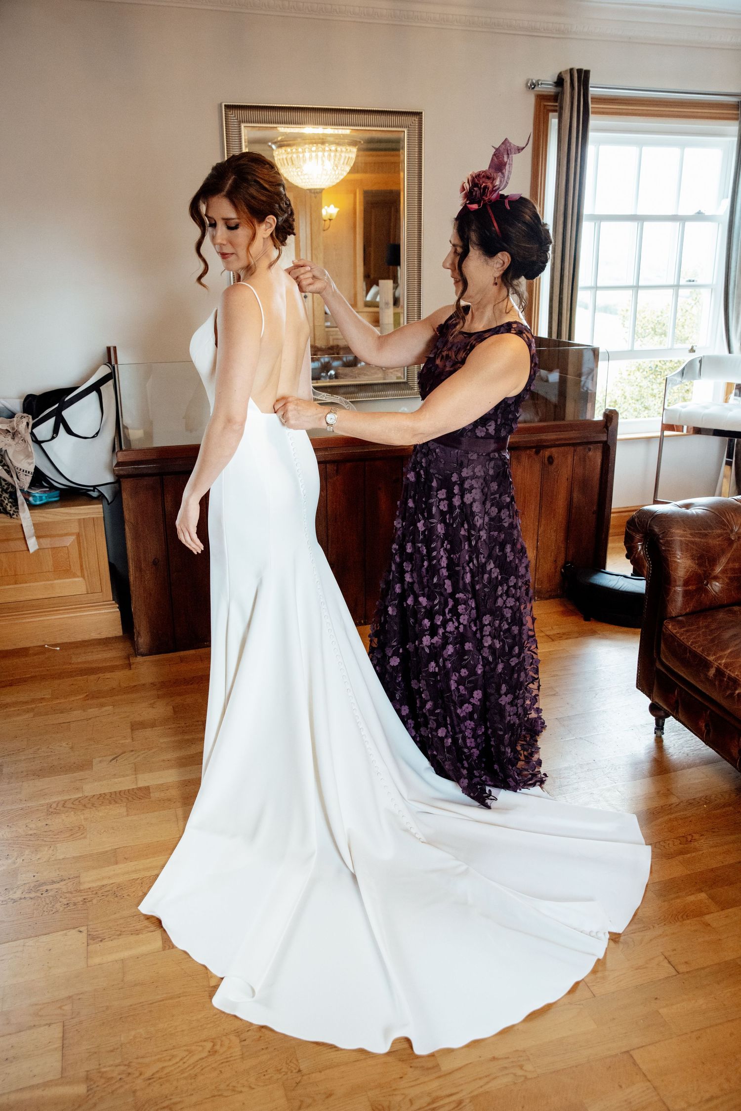 Wedding dress preparation scene with white gown train being adjusted in sunlit room.