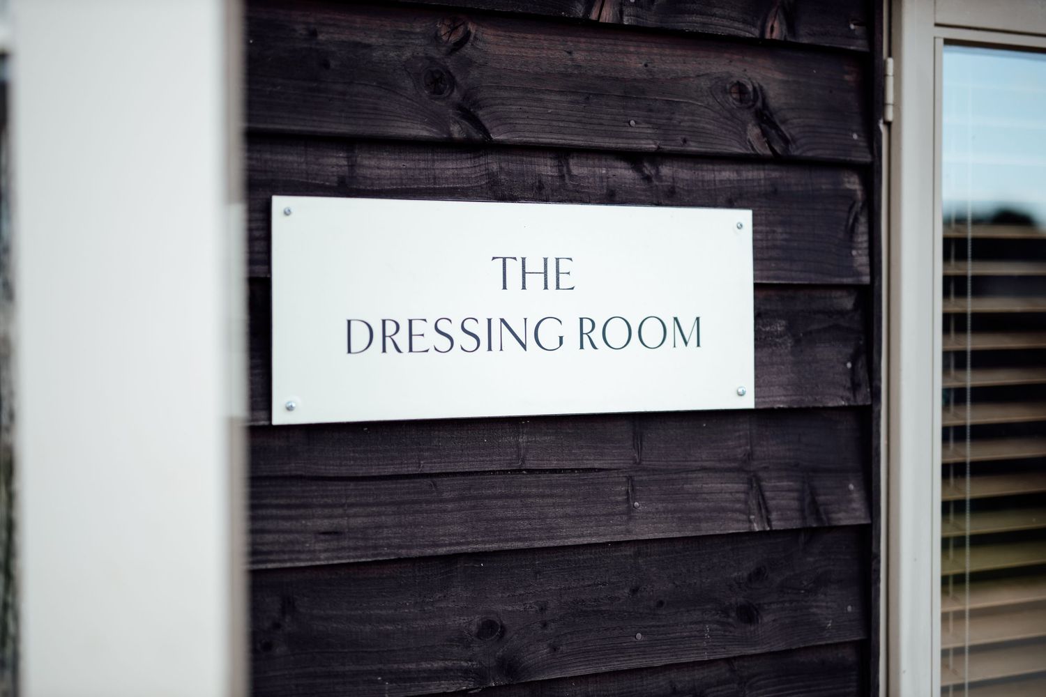 Simple white sign reading 'THE DRESSING ROOM' mounted on dark wooden wall.