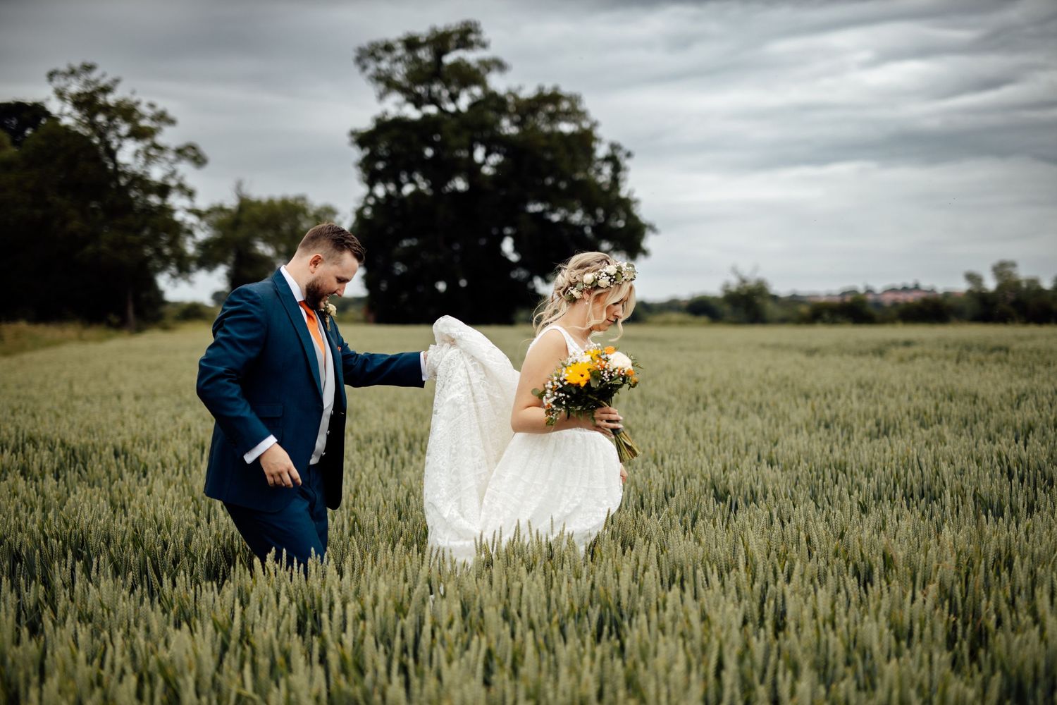 Couple walking through a wheat field on their wedding day with dramatic cloudy sky.