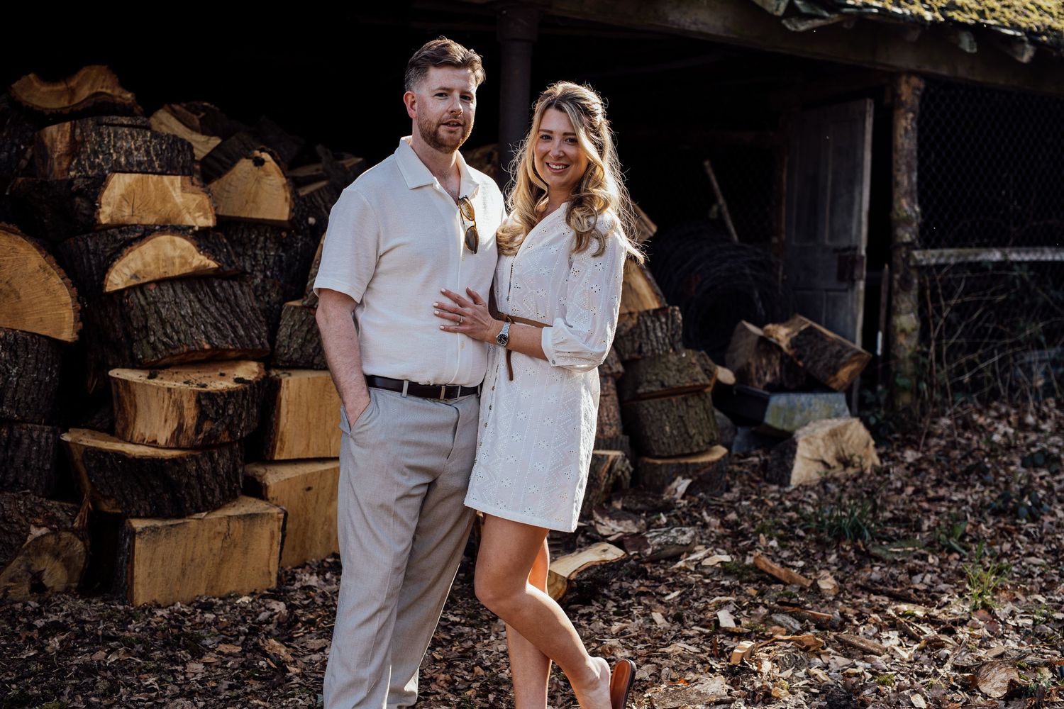 Couple embracing near stacked firewood during outdoor photo session.