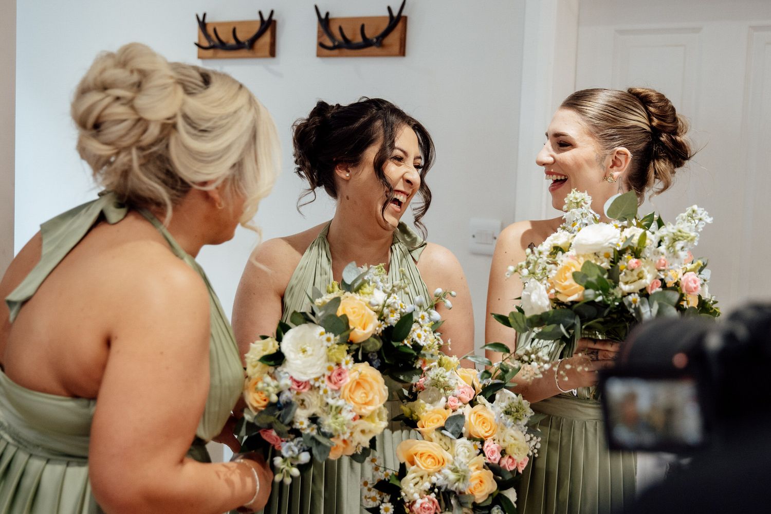 Bridesmaids in sage green dresses holding peach and white bouquets.