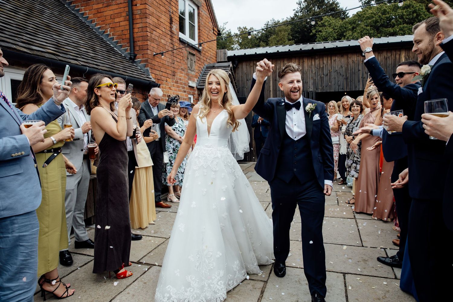 Wedding celebration outside a rustic brick venue with guests throwing confetti.