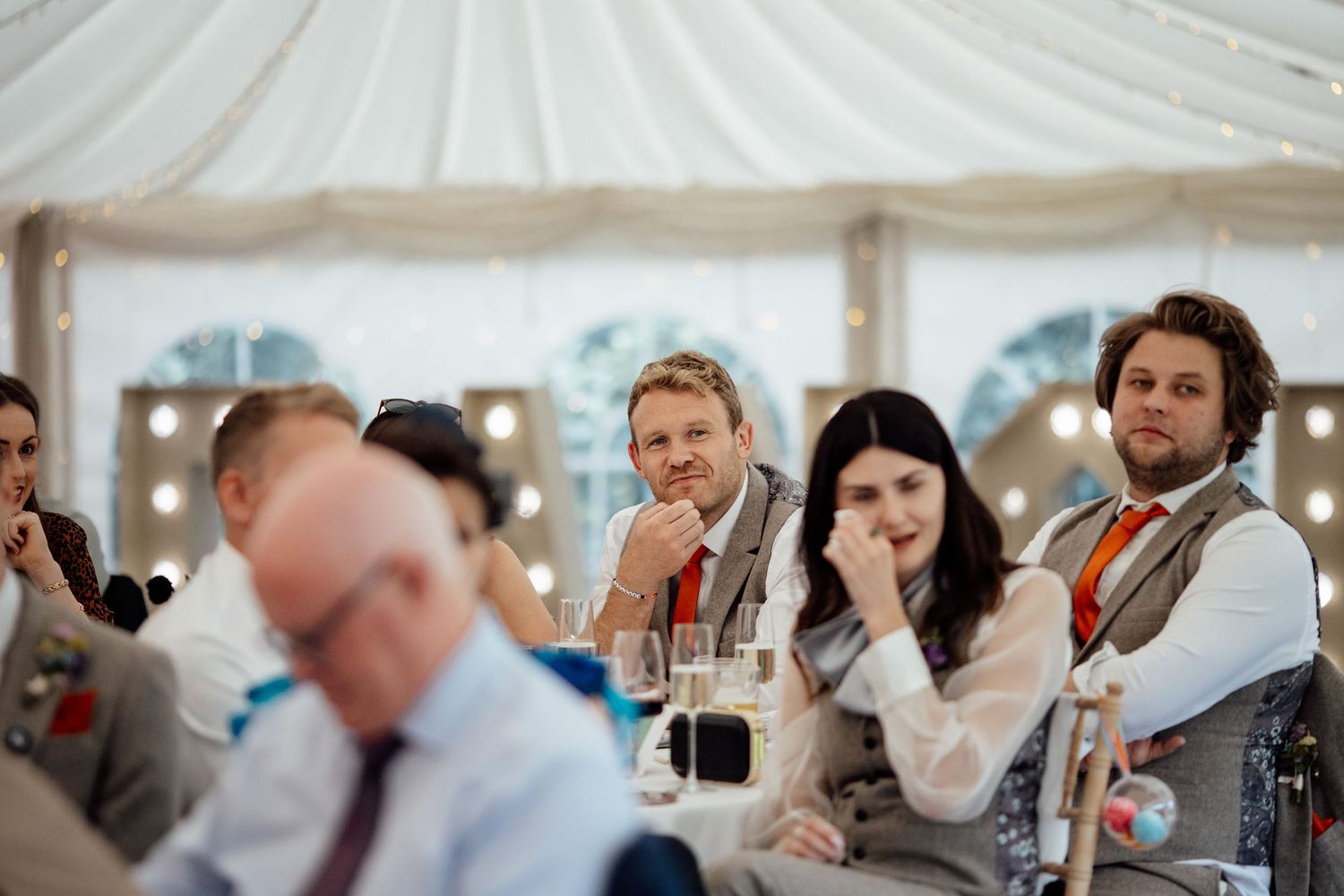 Wedding reception under a white tent with festive string lights and decorations.