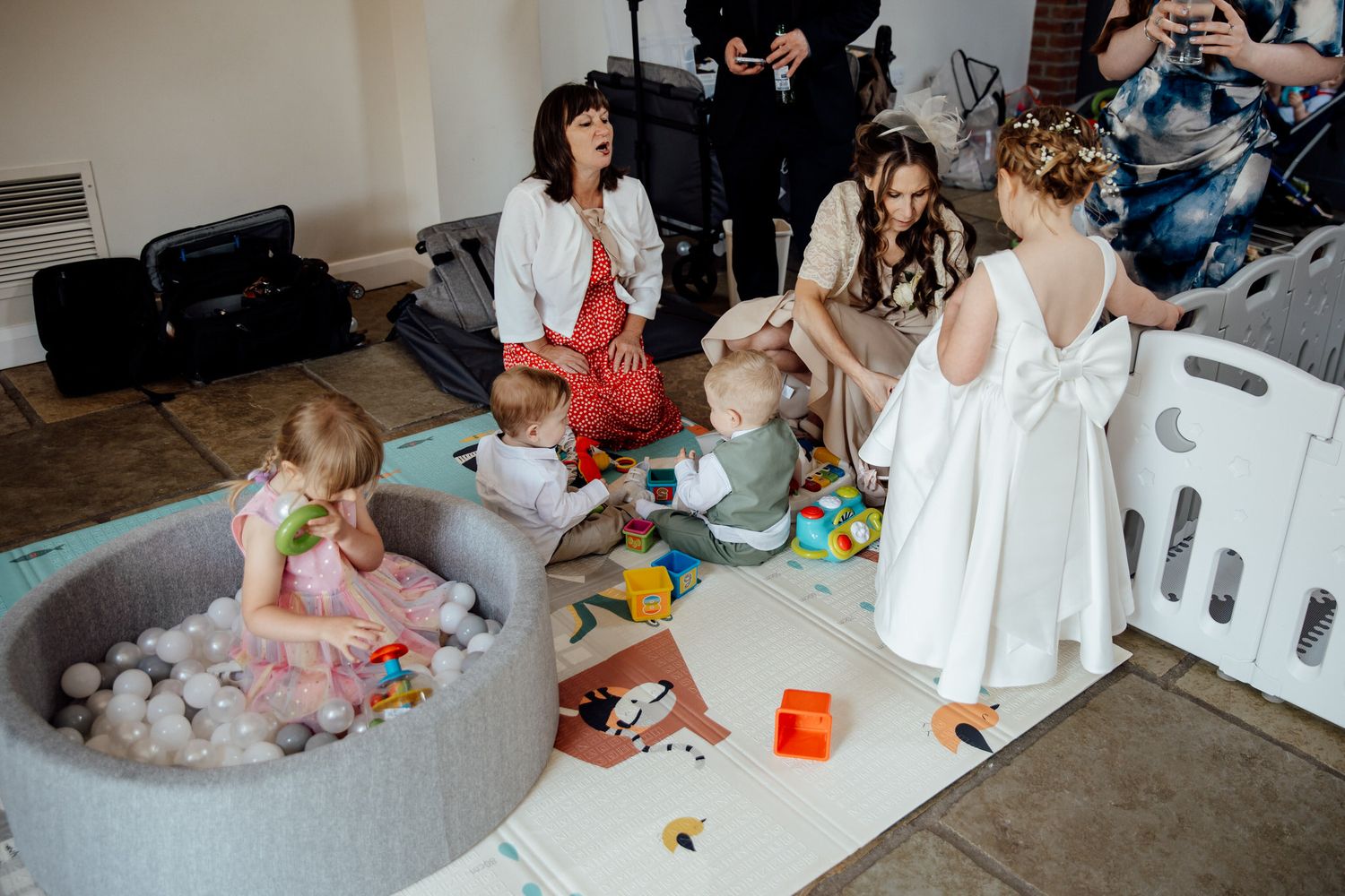 Children play in a ball pit while wedding preparations continue in a modern venue setting.