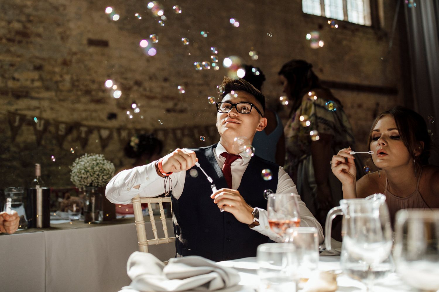 Wedding guests enjoying a meal at tables with elegant place settings and floating bubbles.