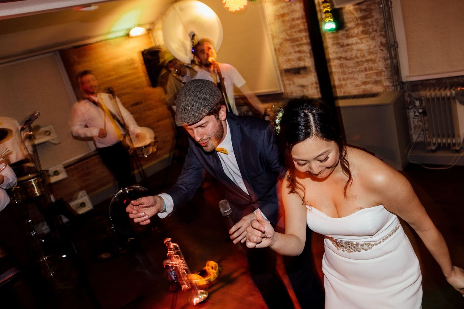 Wedding guests dancing and celebrating at reception venue with warm lighting.