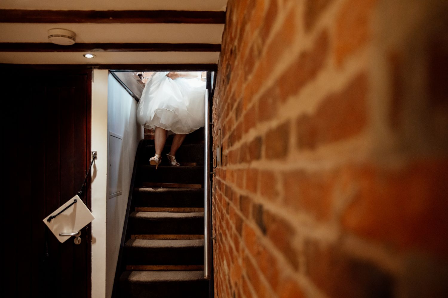 Wooden staircase in rustic venue with exposed brick wall and warm lighting.
