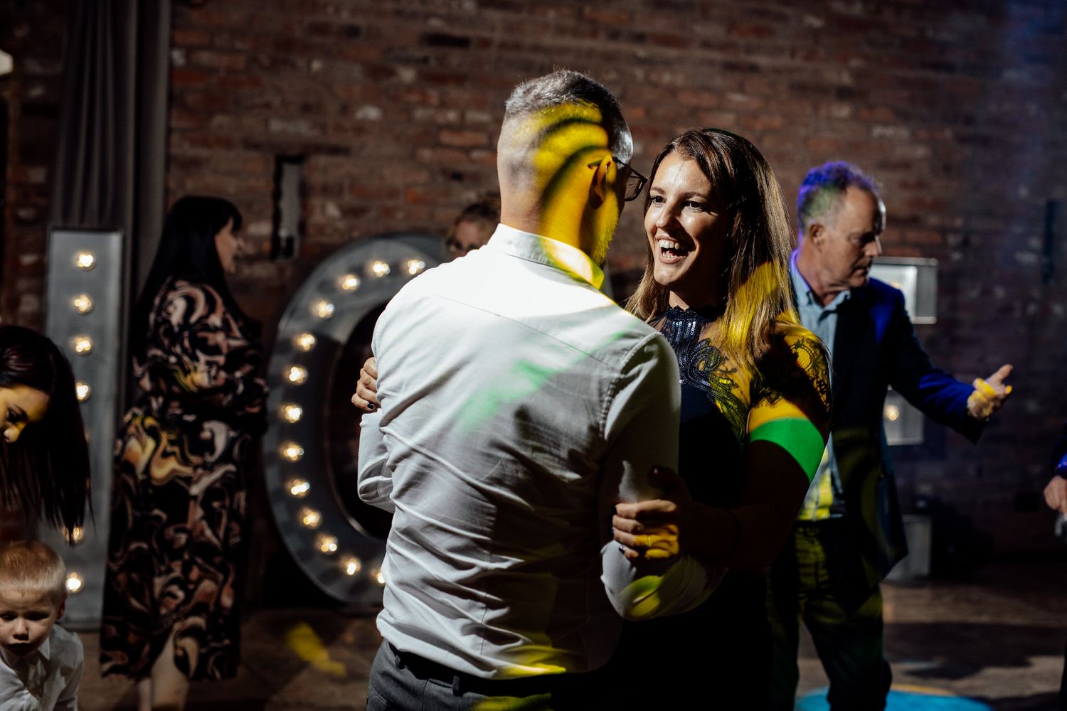 Wedding reception dance party with guests enjoying celebration in brick-walled venue.